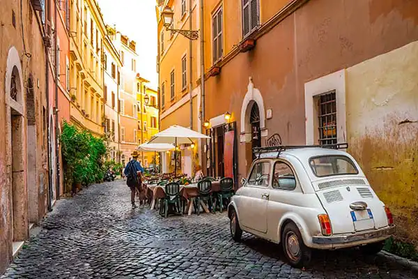 Vicolo di Trastevere con una Fiat 500 d'epoca parcheggiata tra i palazzi
